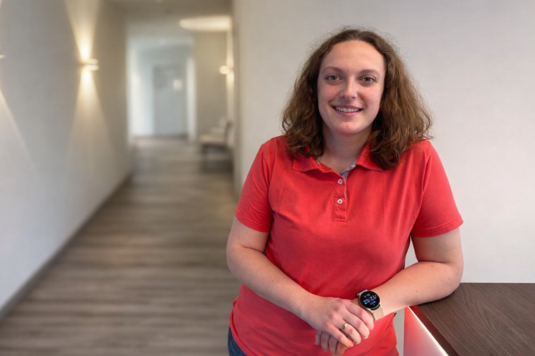 Frau Nowak Junge Frau mit blonden Haaren in einem roten Shirt, lächelt entspannt.